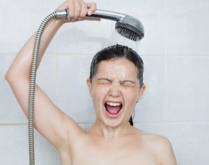 Shocked woman under a cold shower, reacting to lack of hot water, suggesting need for water heater maintenance.